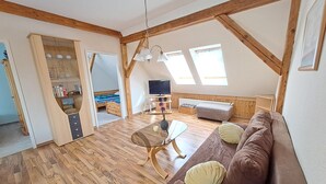 A loft-style room with wooden beams, a glass ceiling, a brown sofa with cushions, a glass coffee table, a television, and a bookshelf. - Vacation apartment 1 (upstairs 1st floor) - Ferienwohnungen Lübs with W-Lan (Lübs)