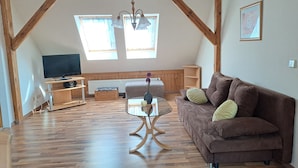 A spacious loft with wooden beams, a brown sofa, a glass coffee table, and a TV on a wooden stand. - Vacation apartment 1 (upstairs 1st floor) - Ferienwohnungen Lübs with W-Lan (Lübs)