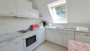 A modern kitchen with white cabinets, a Bosch oven, a red toaster, and a window above the sink. - Vacation apartment 1 (upstairs 1st floor) - Ferienwohnungen Lübs with W-Lan (Lübs)