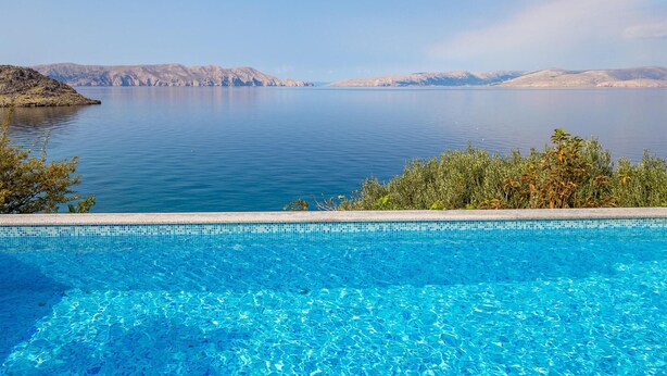 Una piscina azul cristalina con vistas a un lago tranquilo y montañas lejanas.