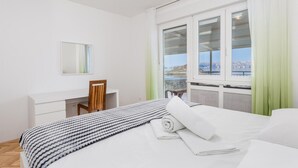 Un dormitorio con cama, escritorio, silla, ventana con vista al mar y espejo en la pared.