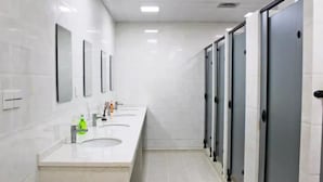 Ein modernes Badezimmer mit drei Waschbecken, Spiegeln und separaten Kabinen.