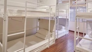 Ein Zimmer mit in Reih und Glied stehenden Etagenbetten, Holzboden und einer weißen Farbgestaltung.