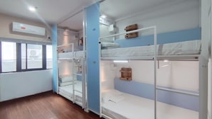 Ein Schlafsaalzimmer mit Etagenbetten, Holzregalen und einem Fenster mit Jalousien.