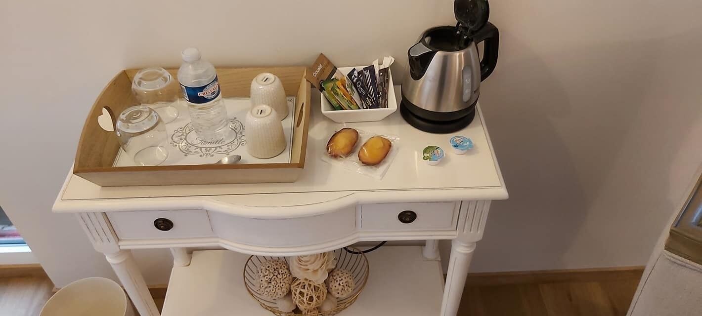 A white wooden table with a tray containing a bottle, glasses, a teapot, and a box of tea bags.