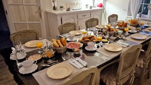 Una mesa lista para el desayuno, con diferentes platos, incluyendo cruasanes, huevos y zumo de naranja.