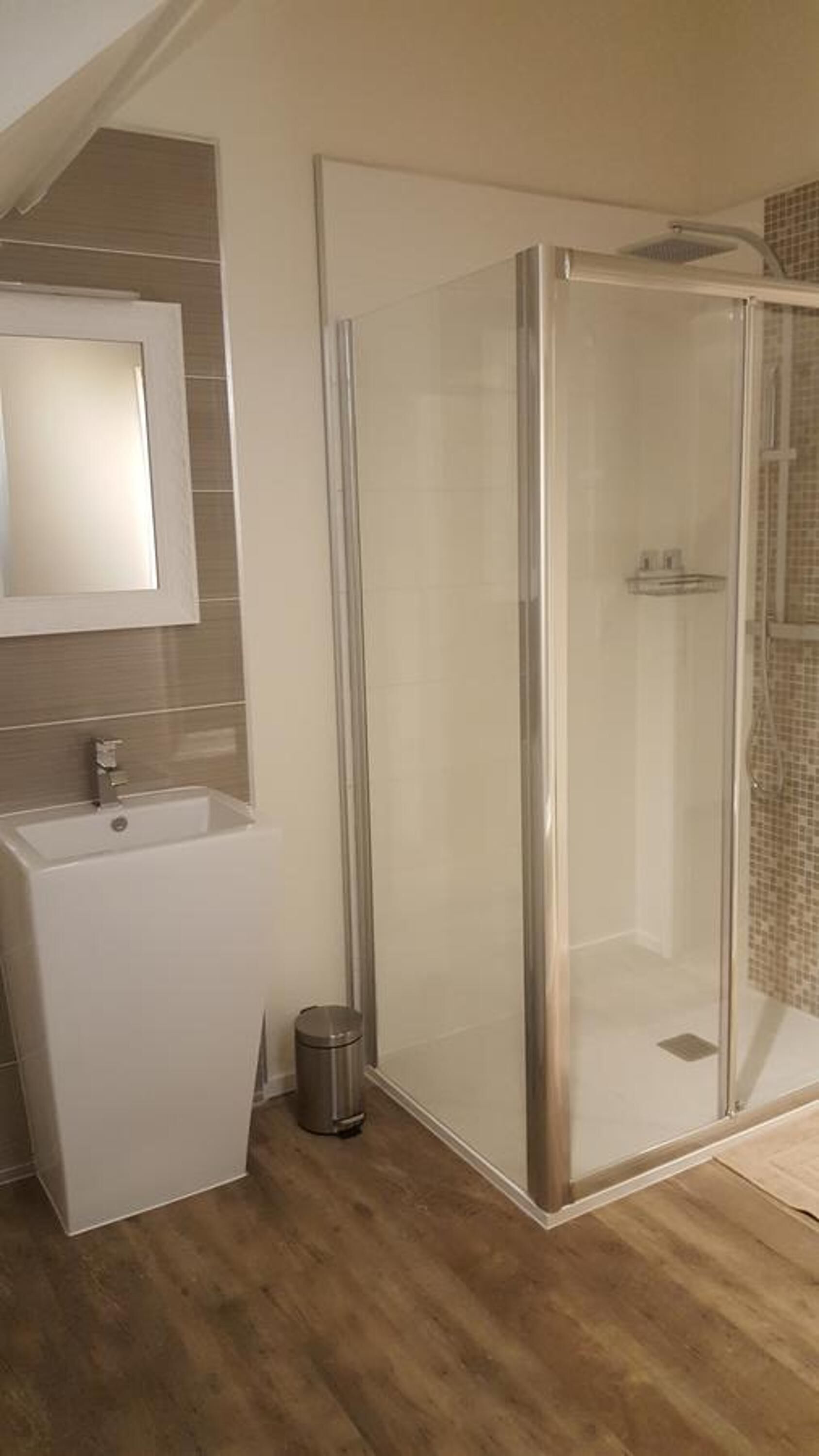 Een moderne badkamer met een douchecabine van glas, een wastafel met spiegel en een prullenbak.