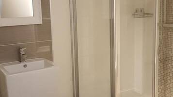 Een moderne badkamer met een douchecabine van glas, een wastafel met spiegel en een prullenbak.