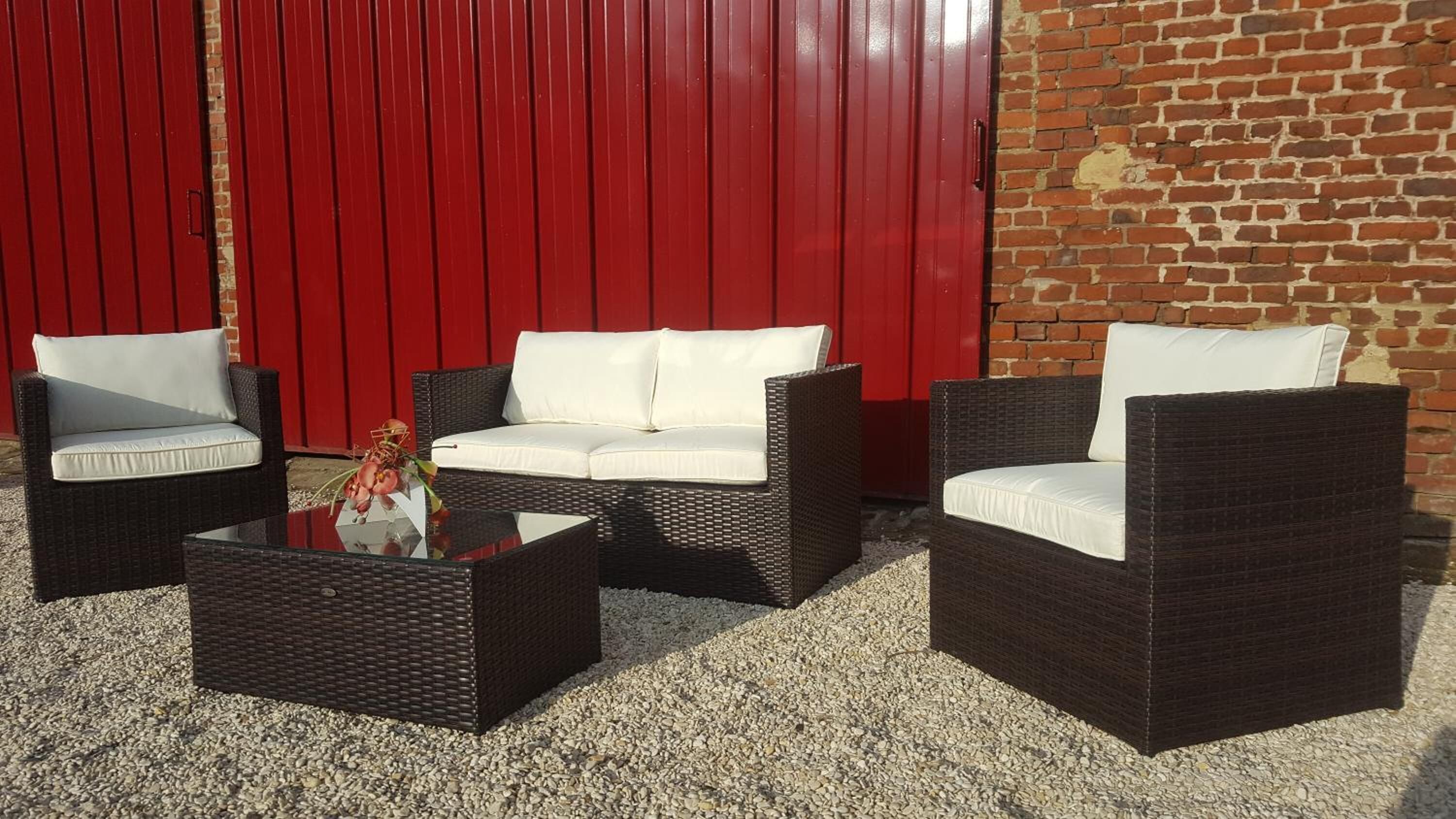 A patio area with wicker furniture, including two armchairs and a sofa, and a small table with a vase.