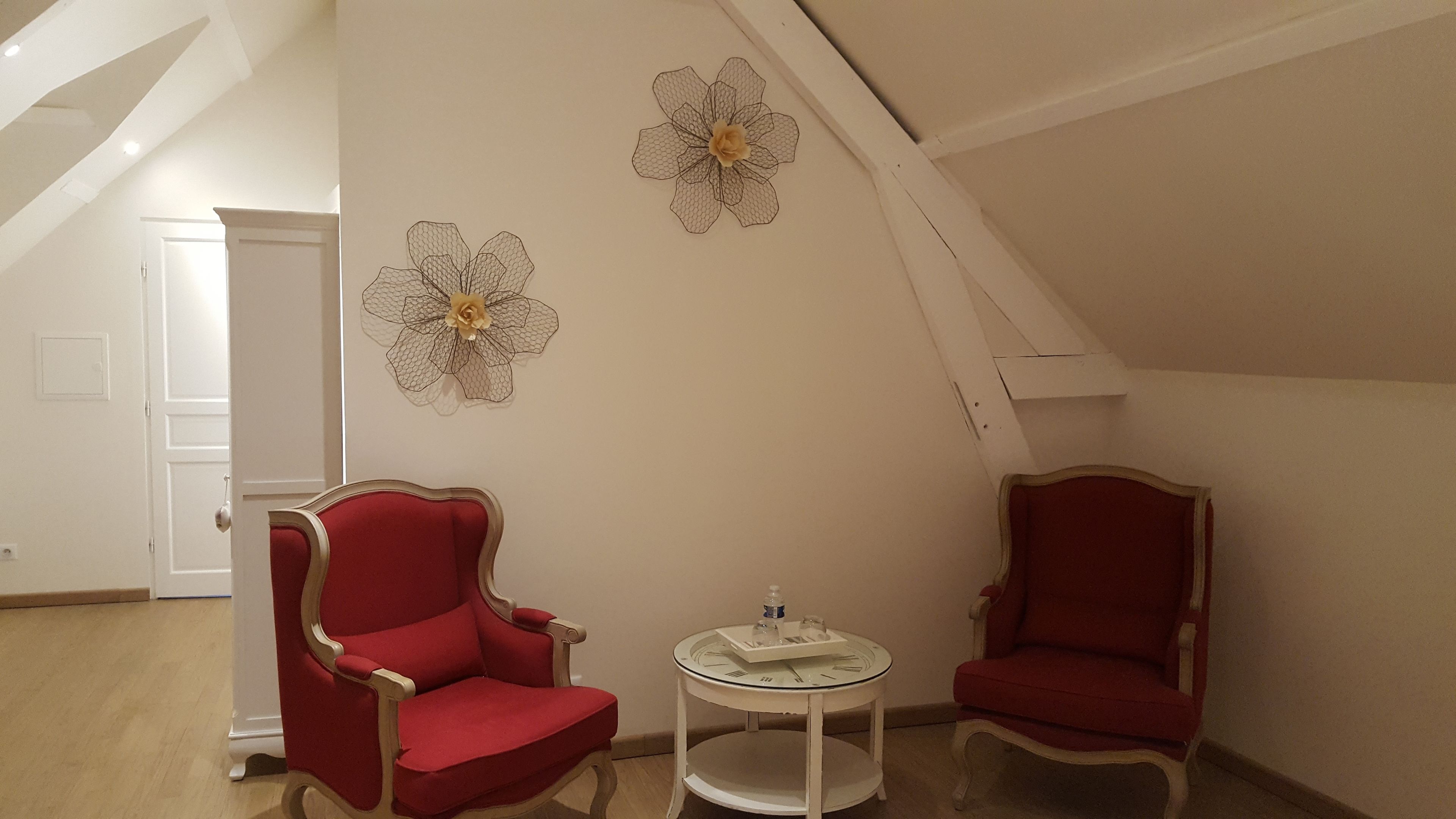 Una habitación con dos sillones rojos, una pequeña mesa redonda con un reloj y dos adornos florales colgados en la pared.