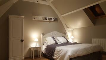 A bedroom with a sloped ceiling, a bed with white and dark bedding, two bedside lamps, a white wardrobe, and a small table with a lamp.