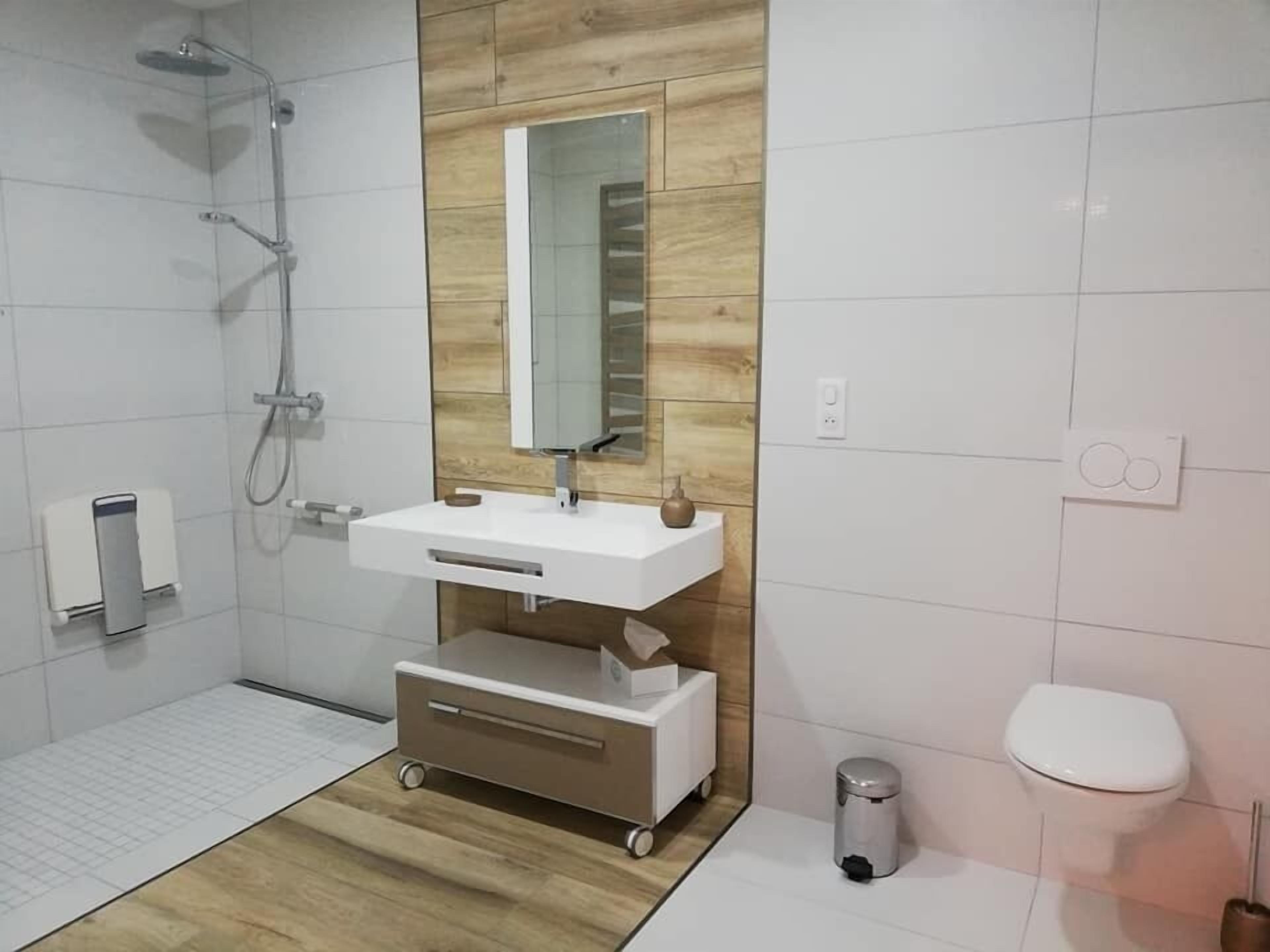 Ein modernes Badezimmer mit Dusche, Waschbecken mit Spiegel, Toilette und Mülleimer.