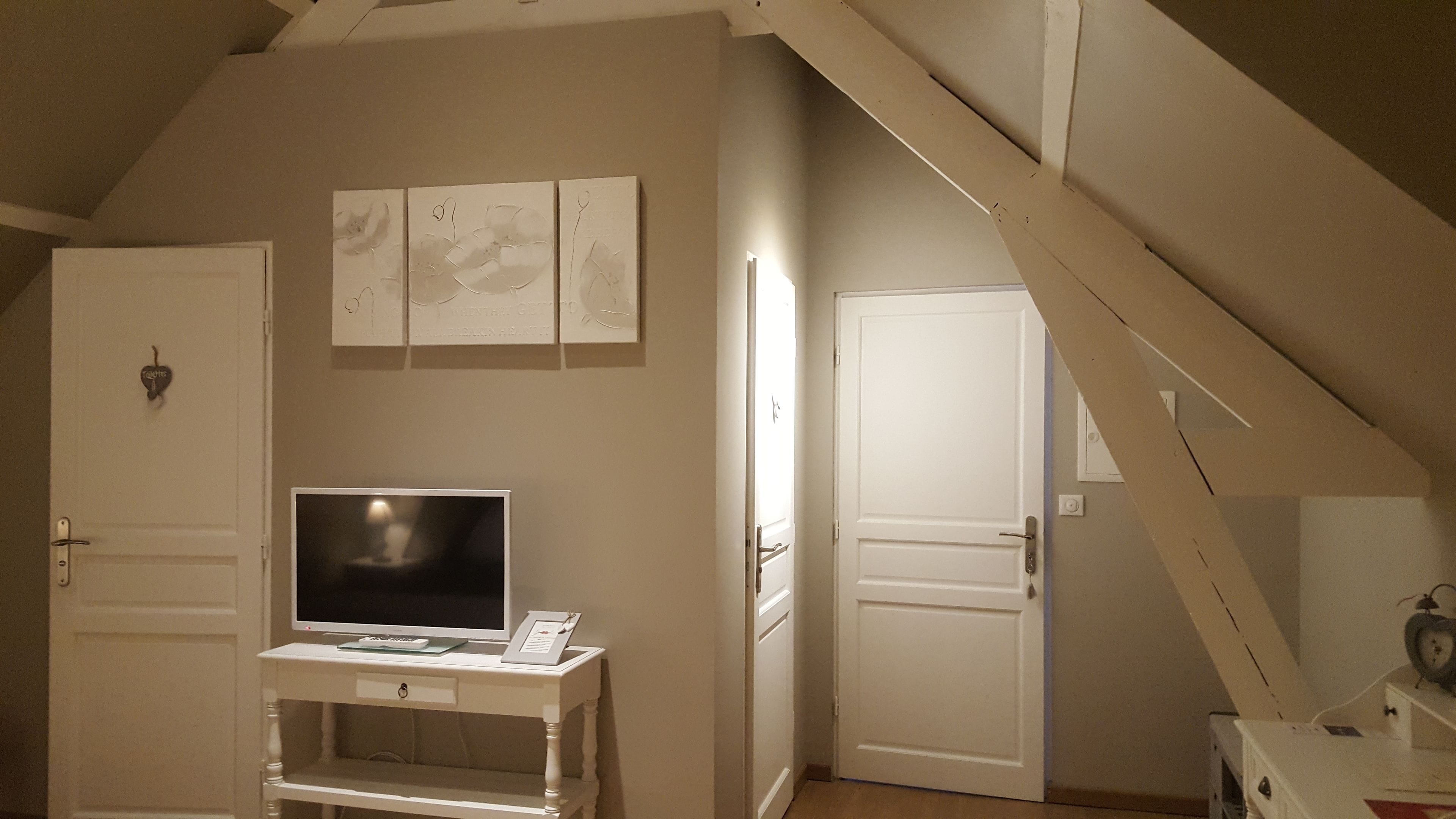 Una habitación con techo inclinado, un televisor sobre un pedestal blanco y tres puertas.