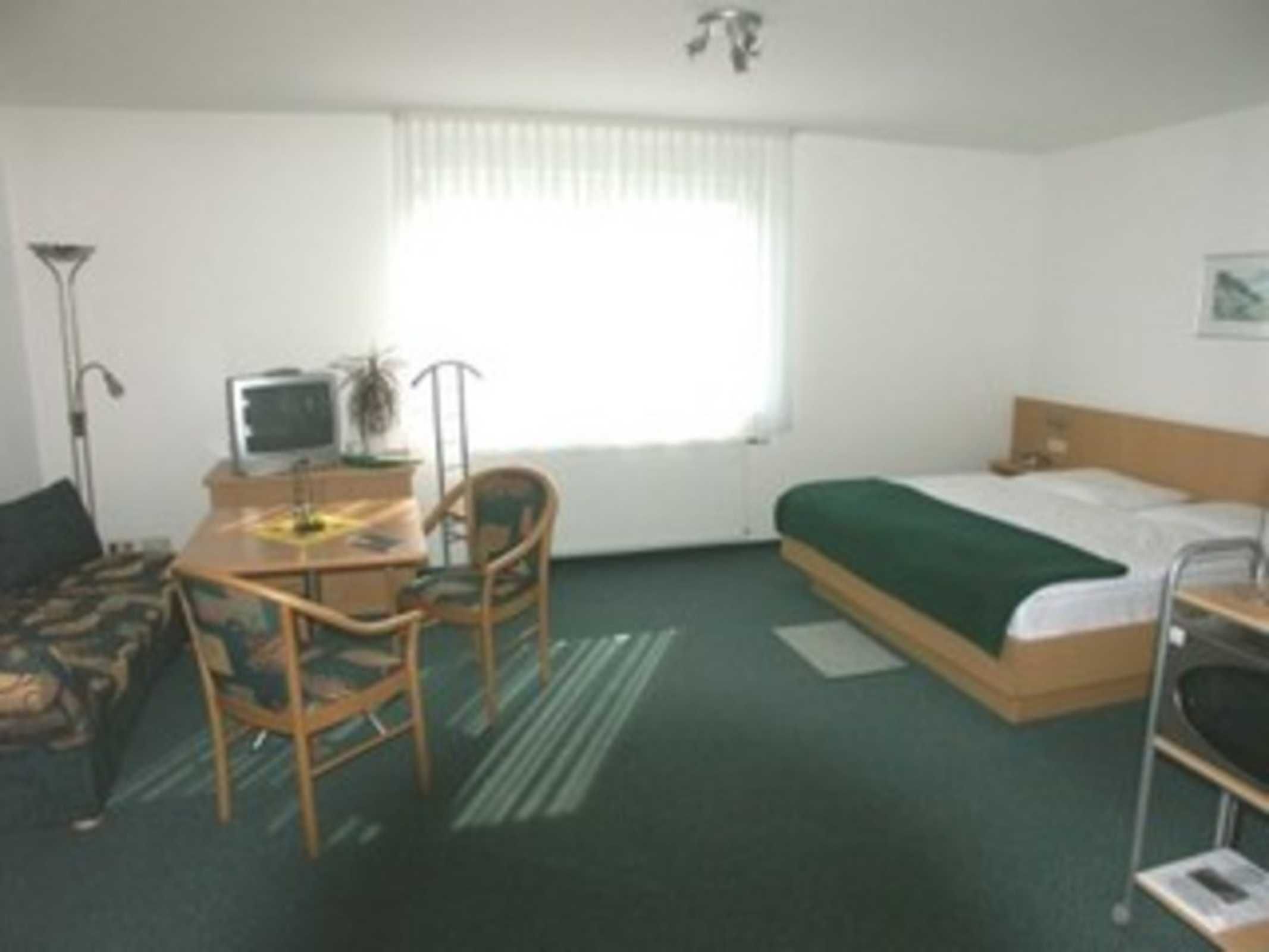 A hotel room with a bed, a desk with a computer, a chair, and a window with curtains.