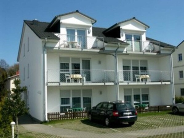 A two-story building with balconies, a car parked in front, and a clear sky.