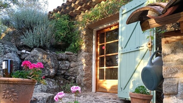 A rustic stone building with a wooden door, potted plants, and a hanging pot. - small, cozy eco-house for environmentally conscious nature-lover (Saint-Roman-De-Codières)