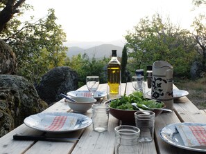 Een picknicktafel buiten, compleet met borden, glazen, een fles olijfolie en een schaal vol groene bladgroenten.