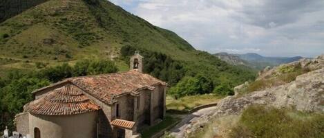 A rural church with a bell tower, surrounded by lush green hills and a clear sky.