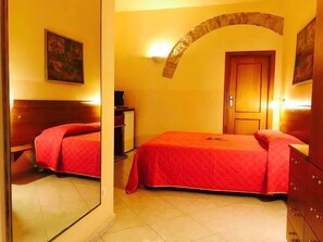 Habitación de hotel con dos camas, un armario de madera, un escritorio pequeño con silla, televisión y un espejo.