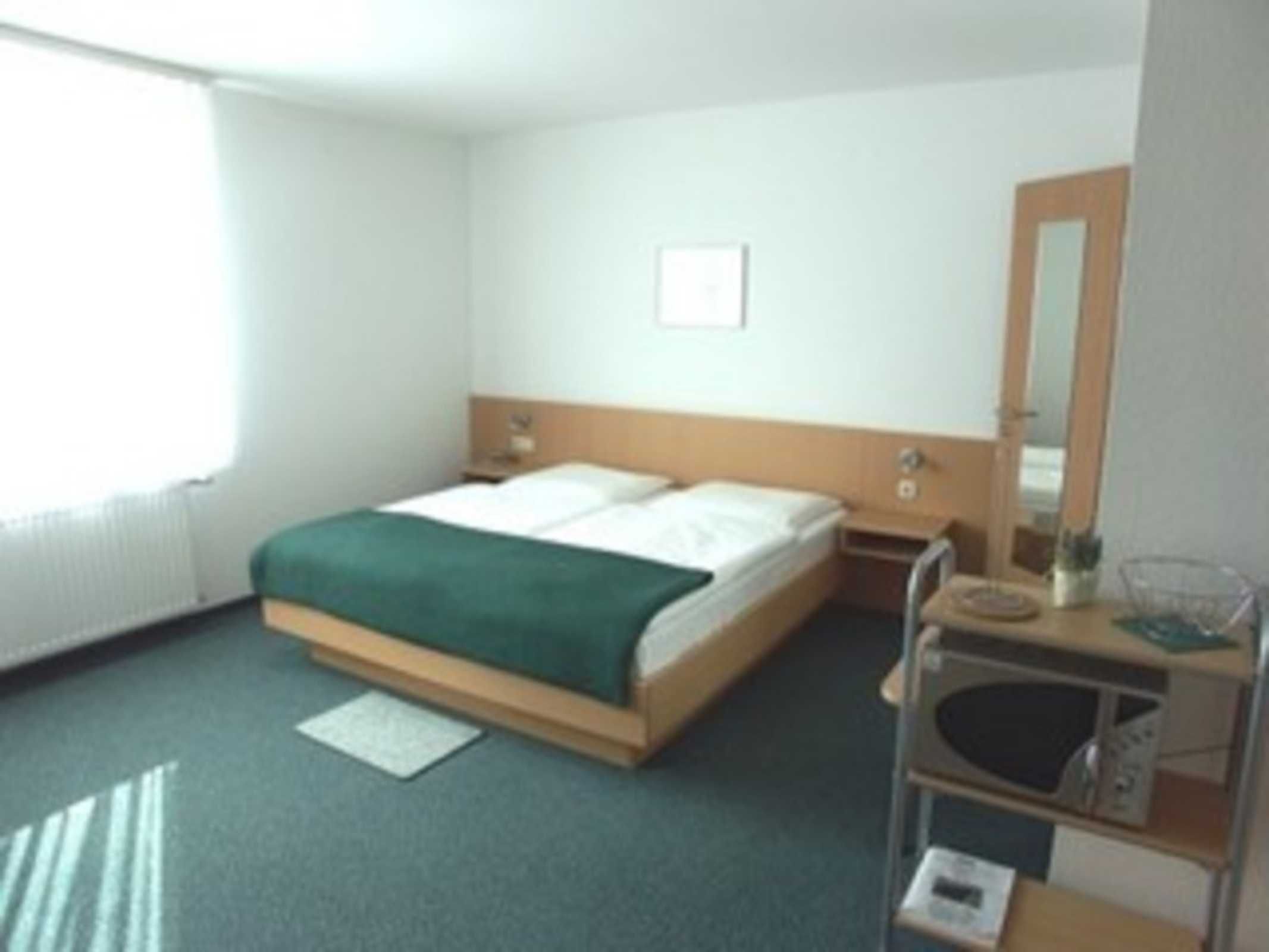 A hotel room with a bed, bedside table, and a mirror.
