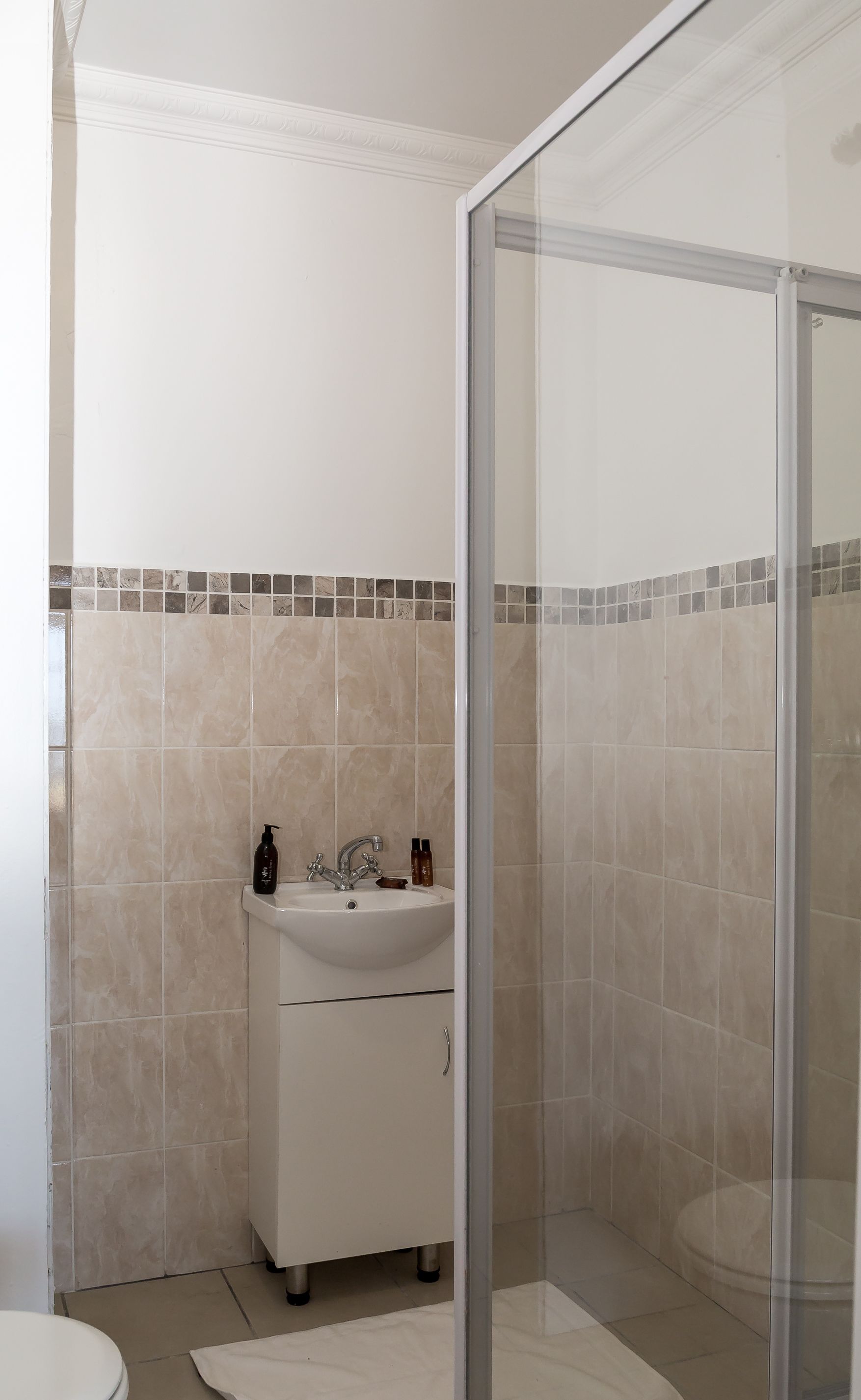 A bathroom with a white sink, a glass shower enclosure, and beige tiled walls.