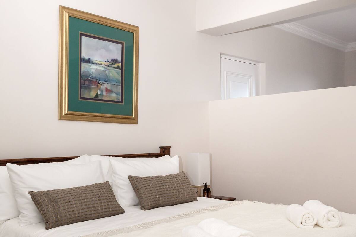 A hotel room with a large bed, a framed picture on the wall, and a view of the outside.