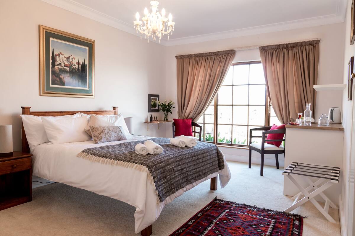 A neatly arranged bedroom with a bed, bedside tables, a chair, a desk, and a window with curtains.