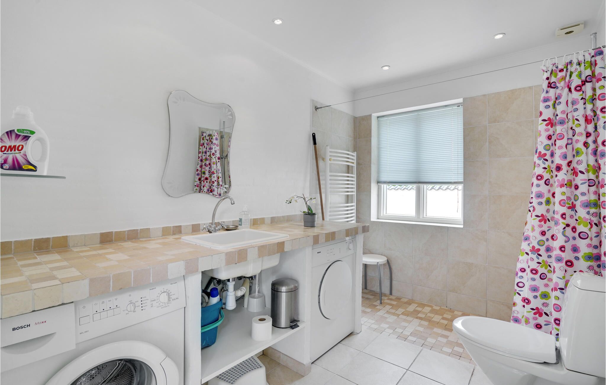 A modern bathroom with a Bosch washing machine, a sink, a mirror, and a shower area.
