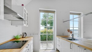 Una cocina moderna con armarios blancos, encimera de madera, un lavamanos y una ventana con vistas a zonas verdes.