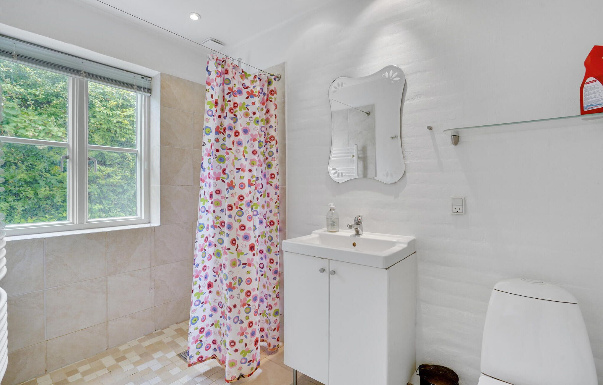 Un baño con ventana, cortina de ducha, lavamanos, espejo e inodoro.