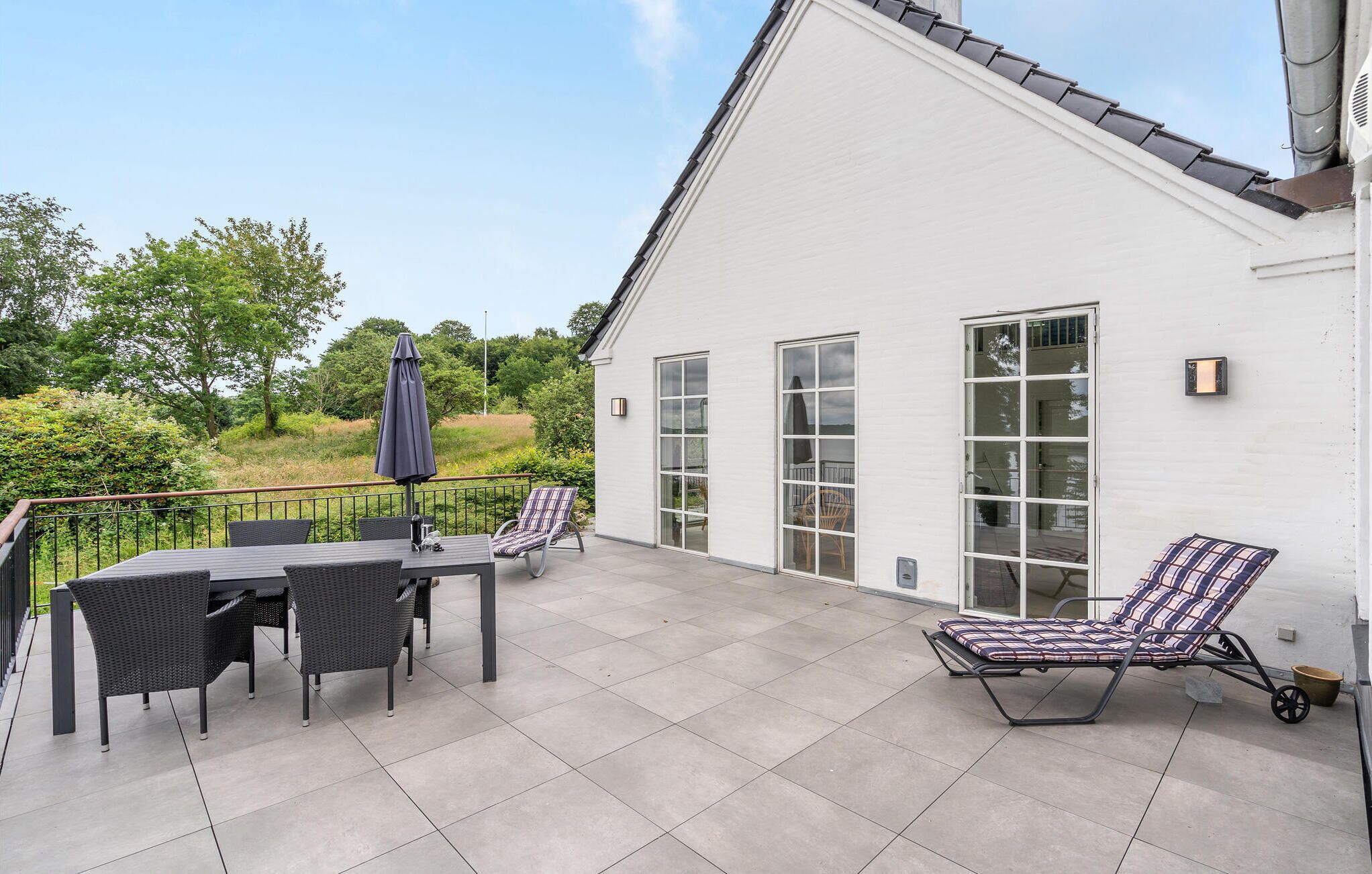 Une terrasse avec une table et des chaises, un fauteuil de relaxation et une grande fenêtre.