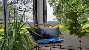 A wicker chair with cushions by a large window overlooking a garden. - Elegant stone house in the countryside with swimming pool (Pressignac-Vicq)