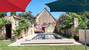 A swimming pool with a stone building in the background, surrounded by greenery. - Elegant stone house in the countryside with swimming pool (Pressignac-Vicq)