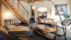 A cozy living room with a wooden staircase, a television on a wooden stand, a rocking chair, and a large painting on the wall.