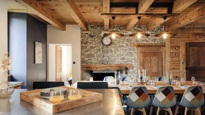 A rustic dining area with a stone wall, wooden beams, and a wooden table set for a meal.