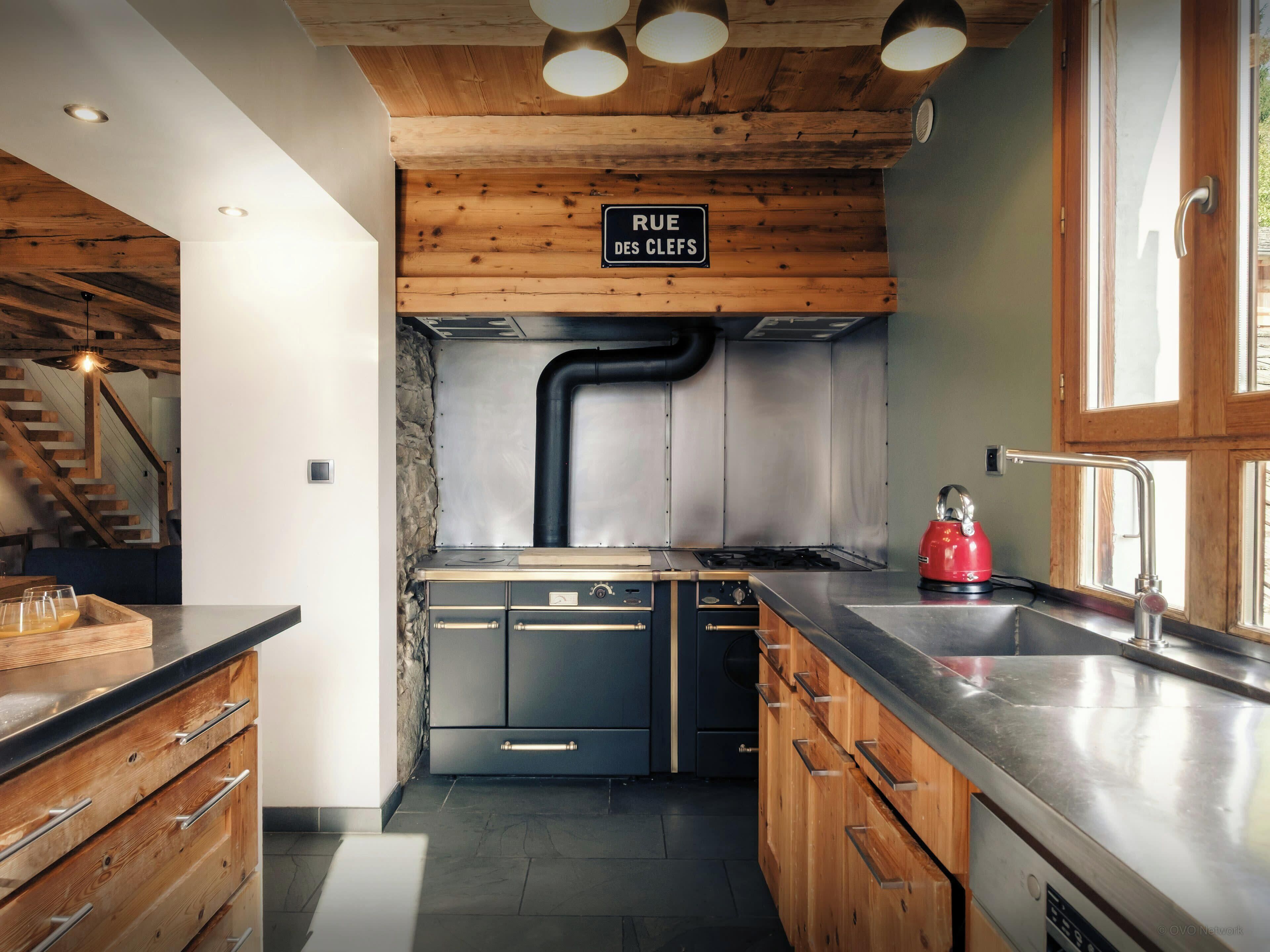Una cucina moderna con mobili in legno, un piano di lavoro in acciaio inox e un condotto a vista.