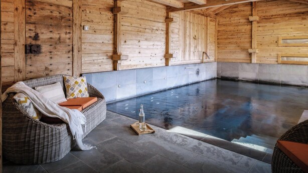 A wooden spa room with a large pool, wicker seating, and a tiled floor.