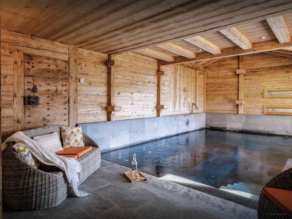 A wooden spa room with a large pool, wicker seating, and a tiled floor.