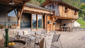 A wooden cabin with a deck, outdoor seating, a bar area, and a view of the surrounding landscape.