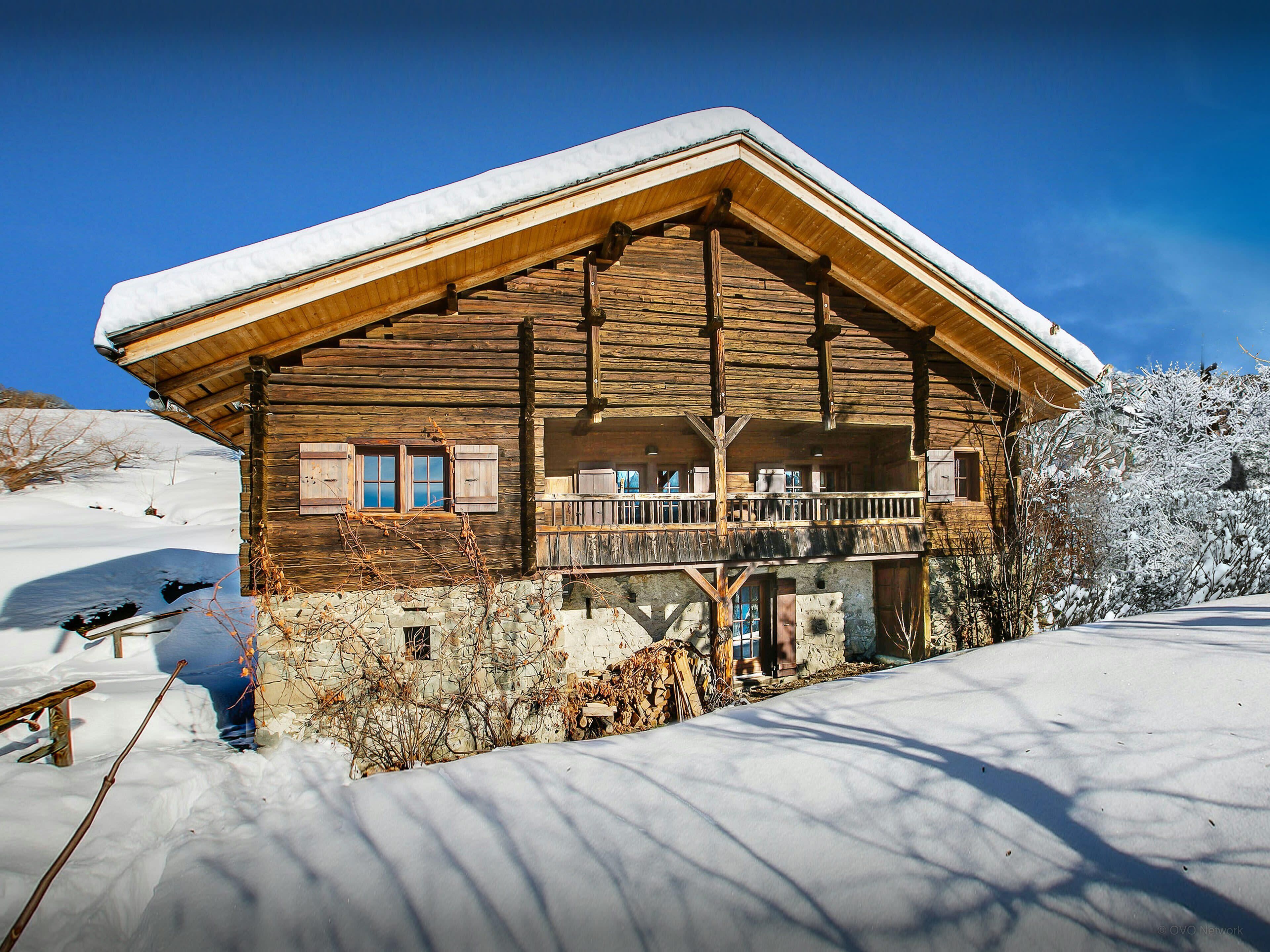 A wooden log cabin with a balcony, surrounded by snow.