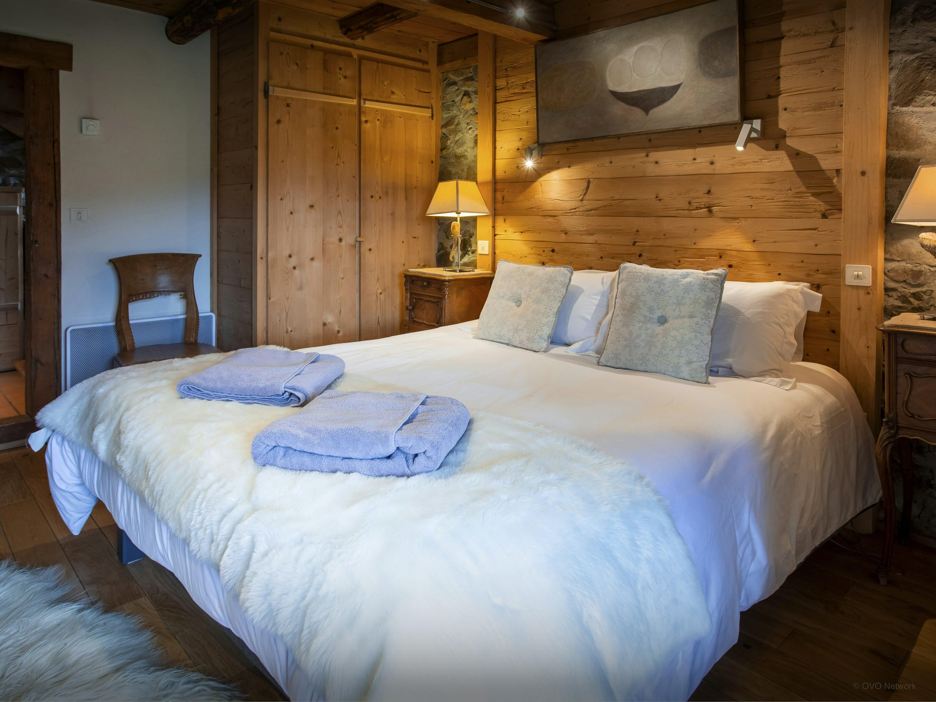 A cozy bedroom with a large bed, wooden walls, a stone accent wall, and a mounted artwork.
