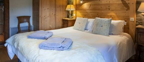 A cozy bedroom with a large bed, wooden walls, a stone accent wall, and a mounted artwork.