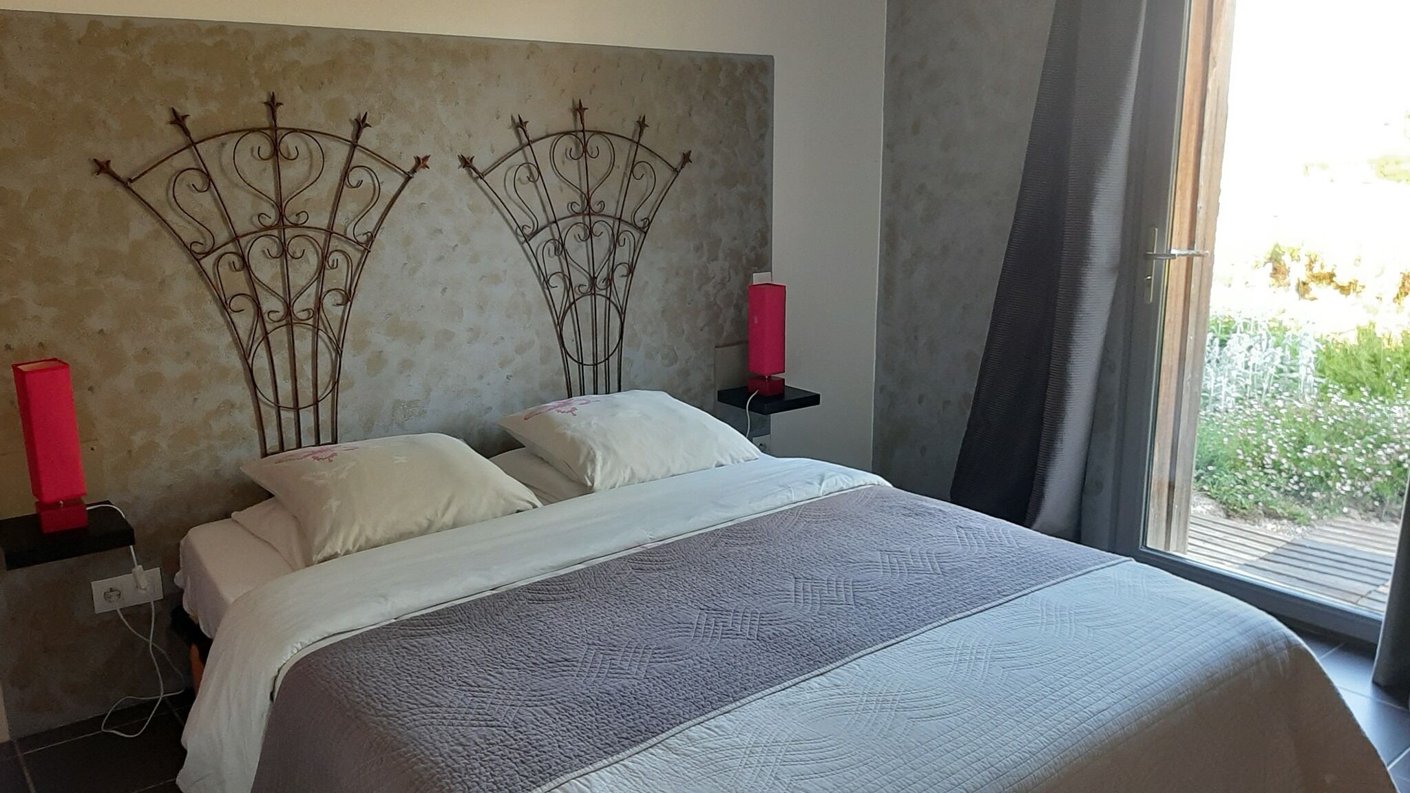 Een slaapkamer met een groot bed, twee nachtkastjes, een rode lamp en uitzicht op groen.