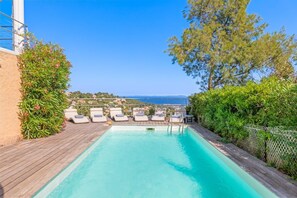 A swimming pool with lounge chairs, surrounded by greenery and overlooking a coastal view.