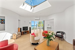 A modern living room with a skylight, a television, a red chair, a wooden table, and a view of the outdoors. - "Calypso House - HYERES (HYERES)