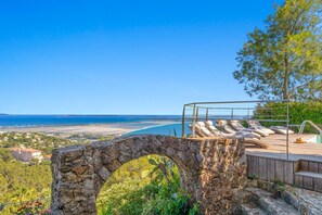 A stone archway leading to a wooden deck with lounge chairs overlooking a coastal view. - "Calypso House - HYERES (HYERES)