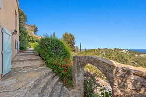 A stone staircase leading to a stone archway, surrounded by lush greenery and a clear blue sky. - "Calypso House - HYERES (HYERES)