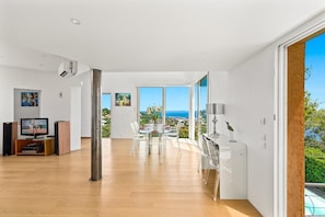 A spacious living area with a large window, a dining table, and a television.