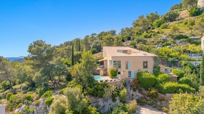 A hillside villa with a swimming pool, surrounded by lush vegetation and rocky terrain.