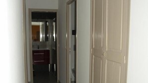 Un pasillo con un armario grande, una puerta que da al baño y una zona de cocina visible al fondo.